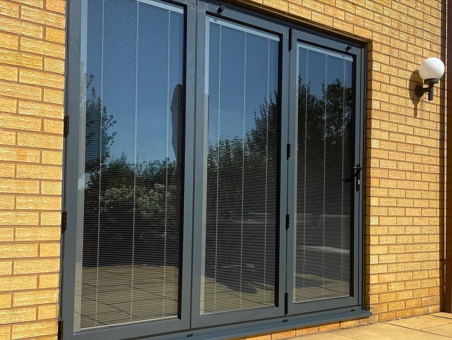 Grey bifold doors set into a yellow brick wall