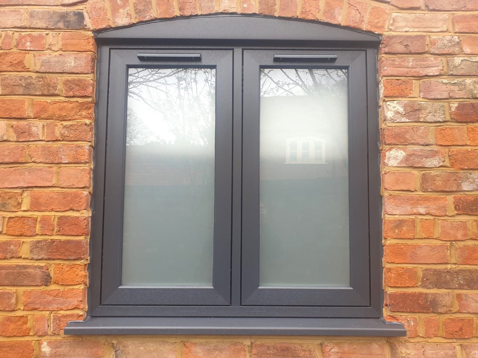 A pair of grey casement windows in a red brick wall