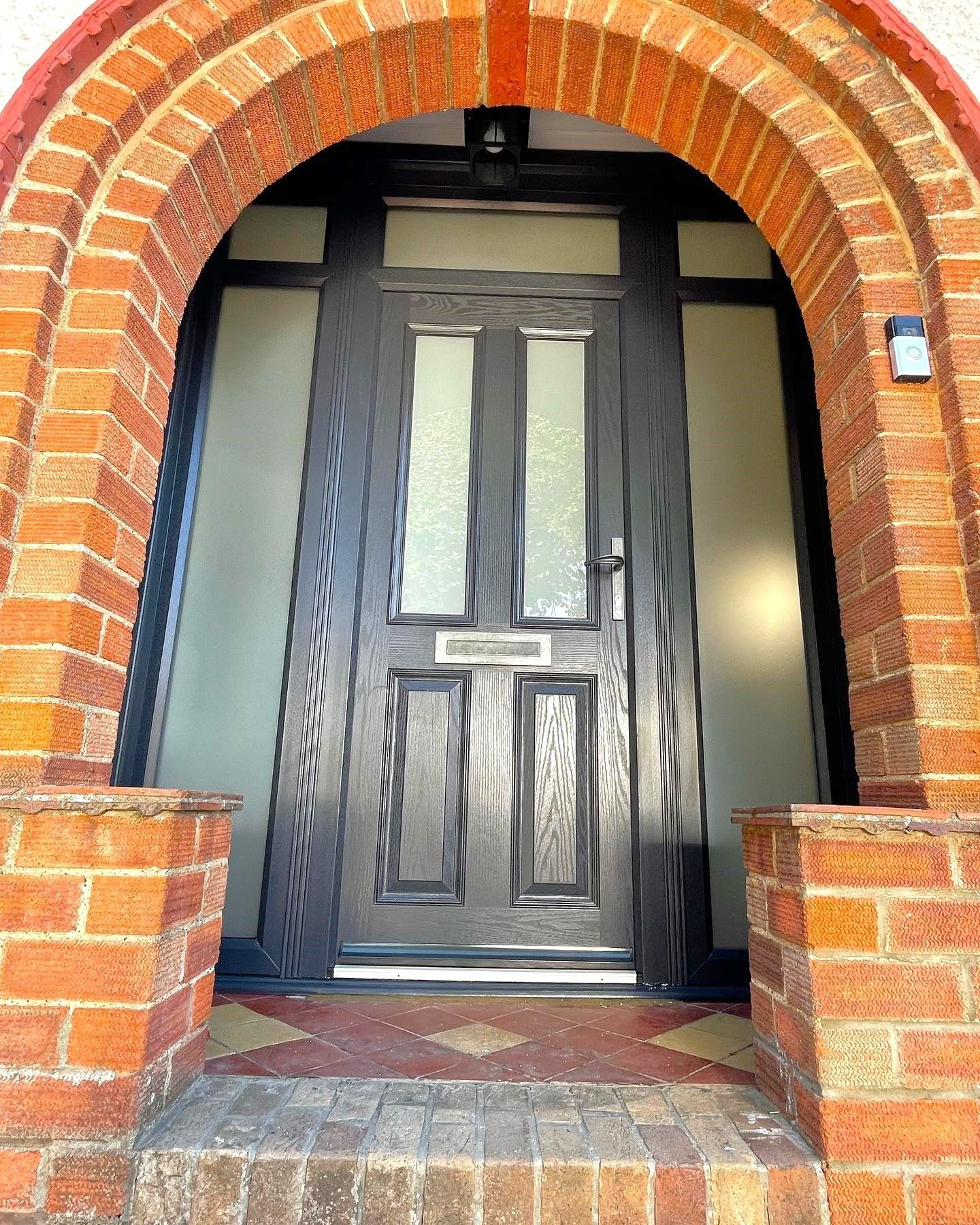 A grey front door with glass panels under a brick arch