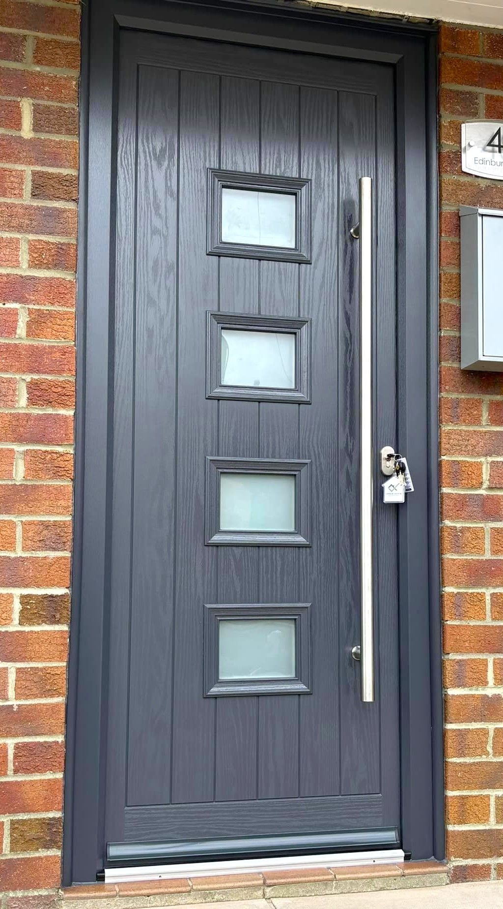 A grey front door with four small glass panels and a long bar handle