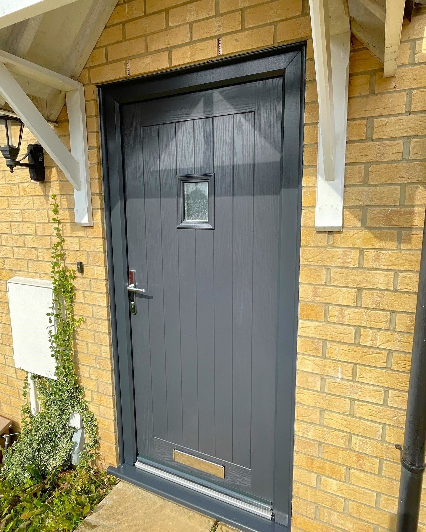 A grey cottage-style front door under a timber canopy