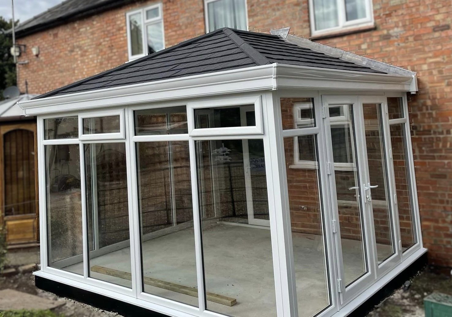 A white conservatory with a grey tiled roof