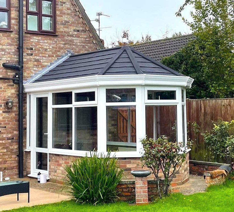 A white conservatory with a grey tiled warm roof