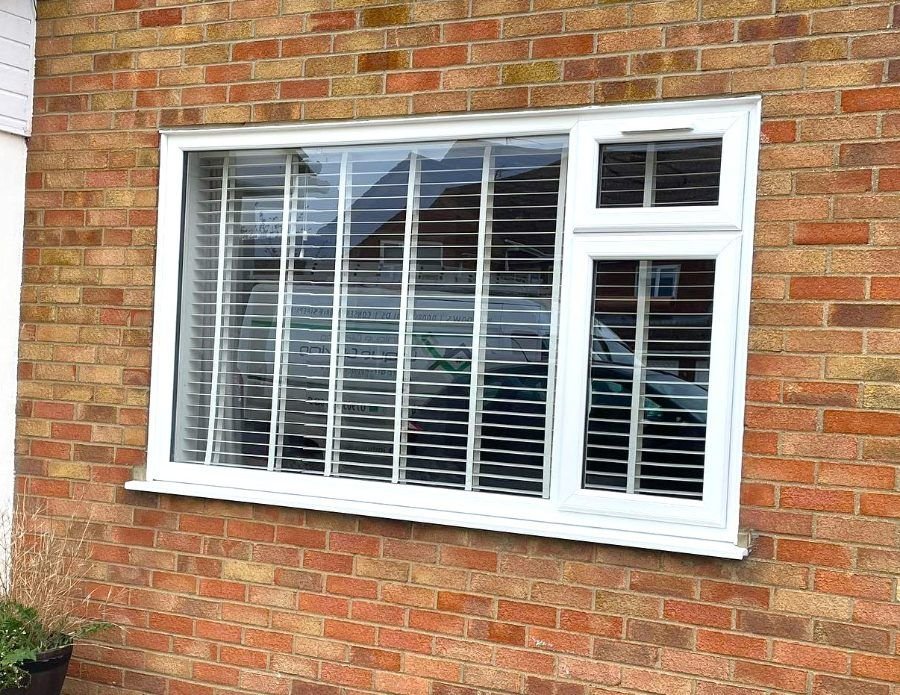 A white casement window in a red brick wall
