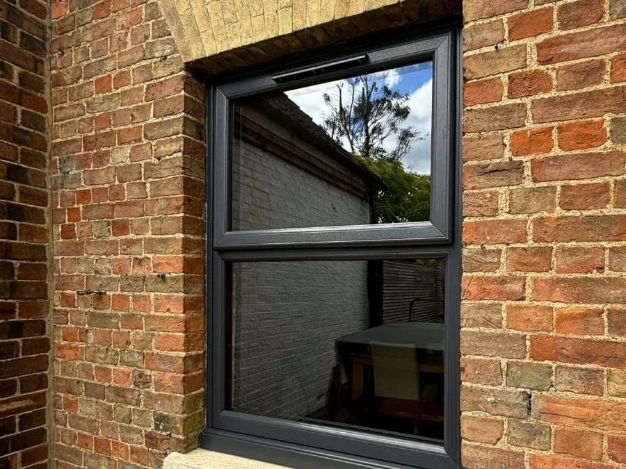 A slim dark grey window in a brick wall